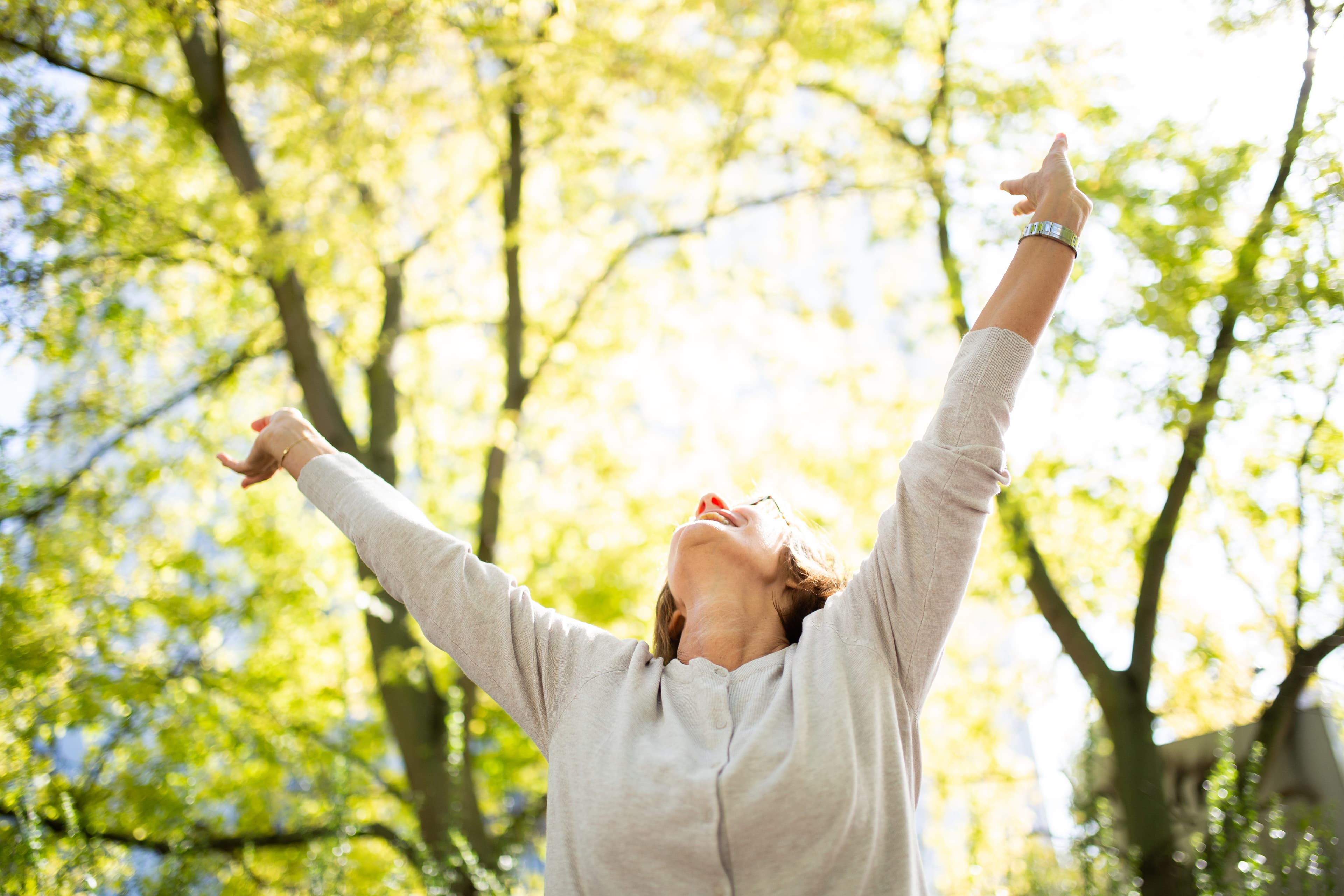 A woman standing outdoors with her arms raised toward the light