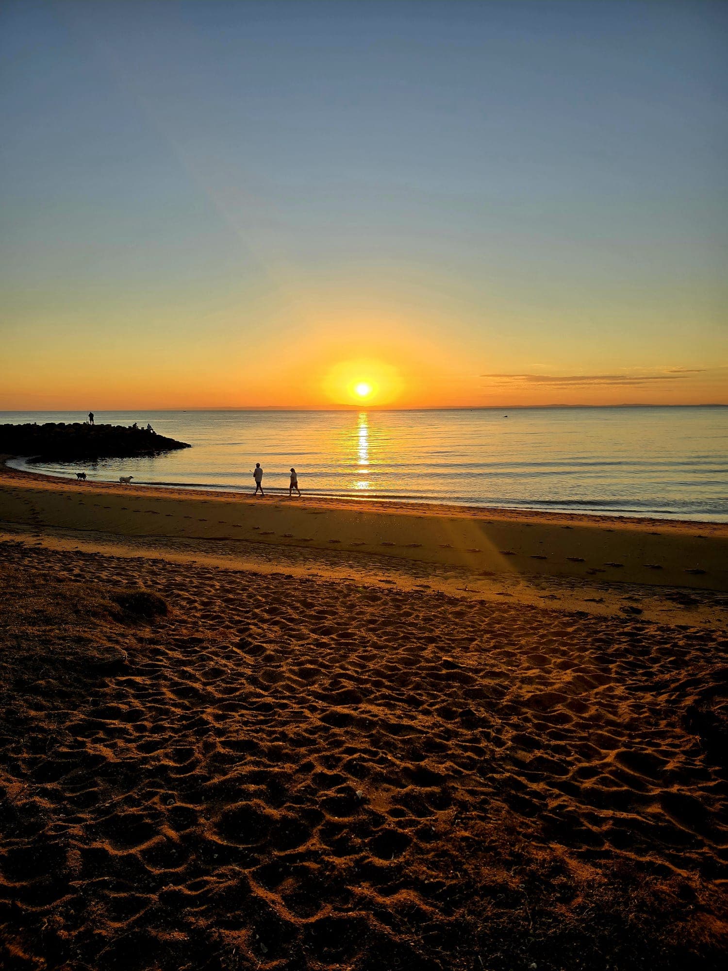 Sunrise over a quiet beach, two people walking along the shoreline